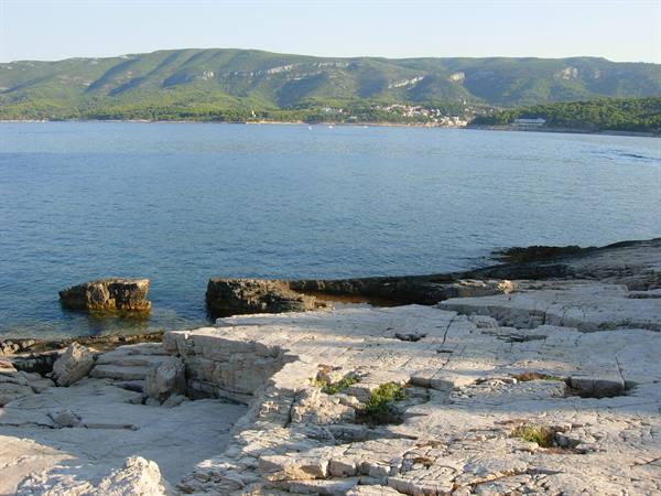 White limestone rocks, calm blue sea, green hills with village in the distance