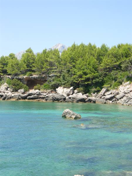 Turquoise water with a rock, green pines on cliffs, mountain behind