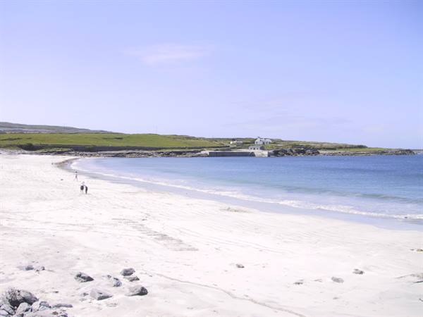Pale sandy beach, two people walking near the water under blue sky