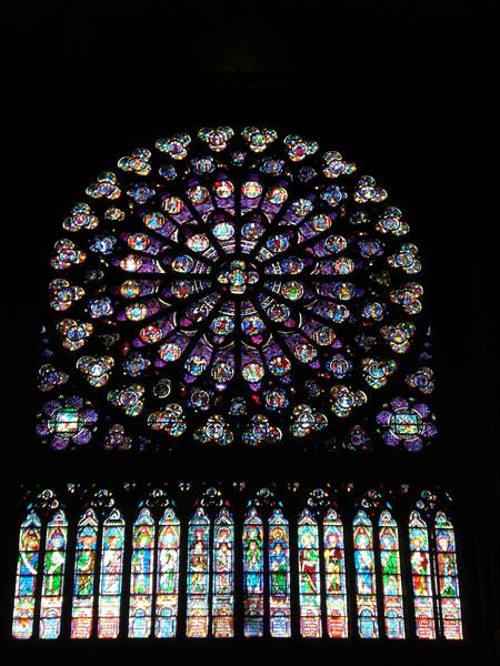 Stained glass rose window of Notre-Dame cathedral, light glowing in darkness