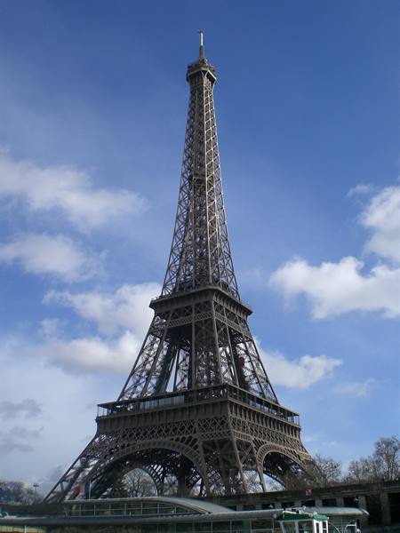 The wrought-iron Eiffel Tower against a blue sky with clouds
