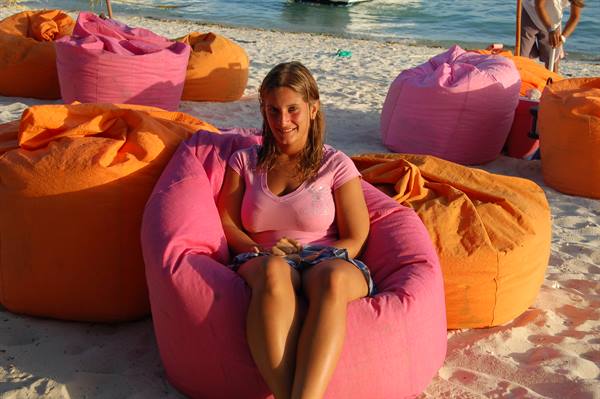 Smiling woman sitting on pink beanbag chair on white sand beach