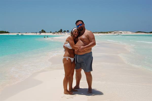 Couple hugging in swimwear on white sand, turquoise water and boats offshore