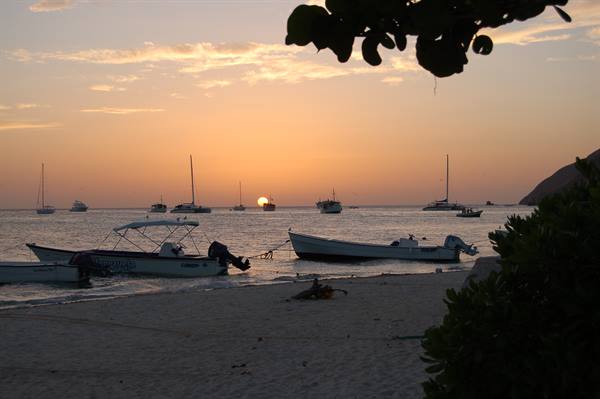 Boats anchored on the sand facing the sea as the sun sinks