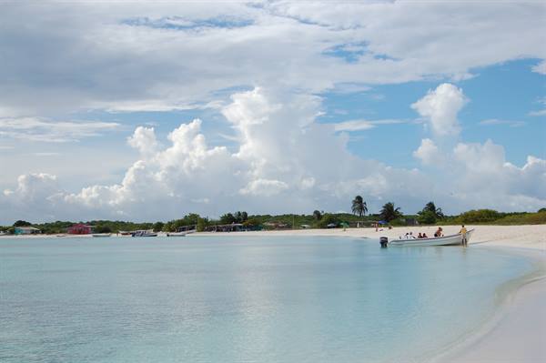Boat with tourists on white sand beach, turquoise water and clouds