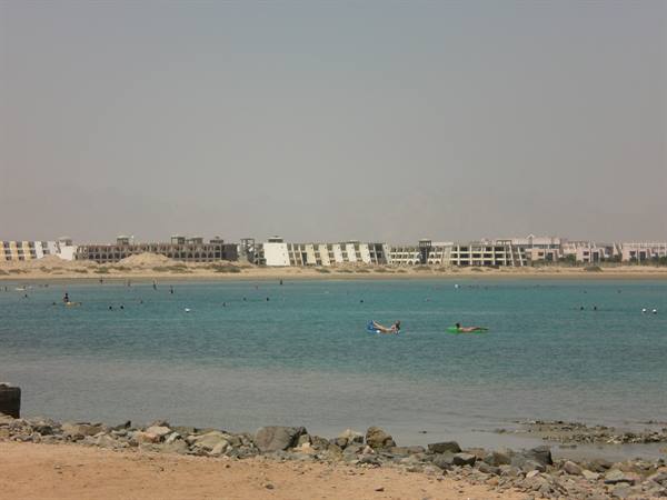 Swimmers on colorful inflatables in turquoise water, hotels along sandy shore