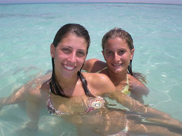 Two smiling girls in clear turquoise sea, bikinis, wet hair, bright sunlight