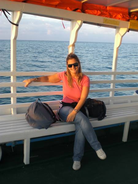 Woman in pink shirt and sunglasses sitting on white boat bench, open sea