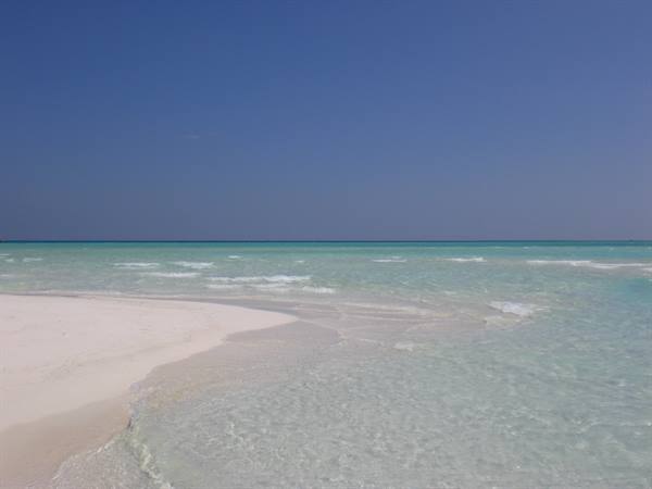 White sand and shallow turquoise water with foam, blue sky