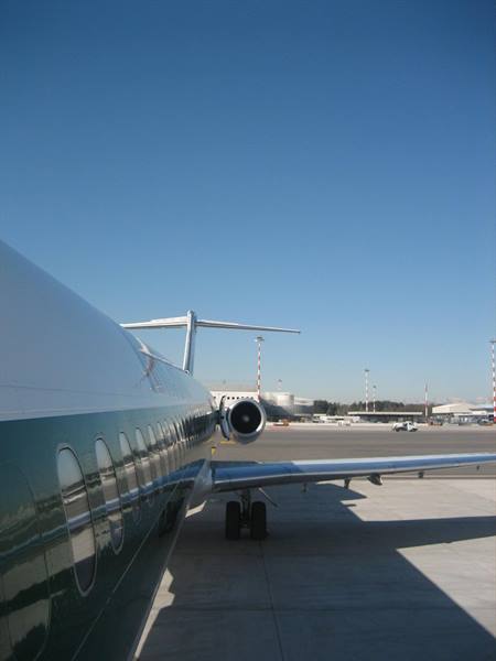 Green passenger jet fuselage parked on airport tarmac under clear blue sky