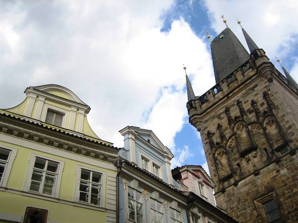 Stone Gothic tower beside colorful yellow, blue and pink facades in Prague