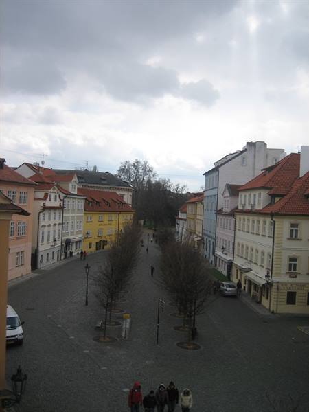 Cobbled square with colorful houses and red roofs under cloudy sky, Prague
