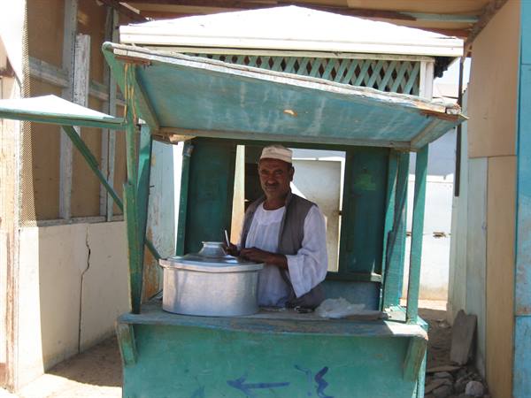 Man in white turban selling tea from a green wooden kiosk