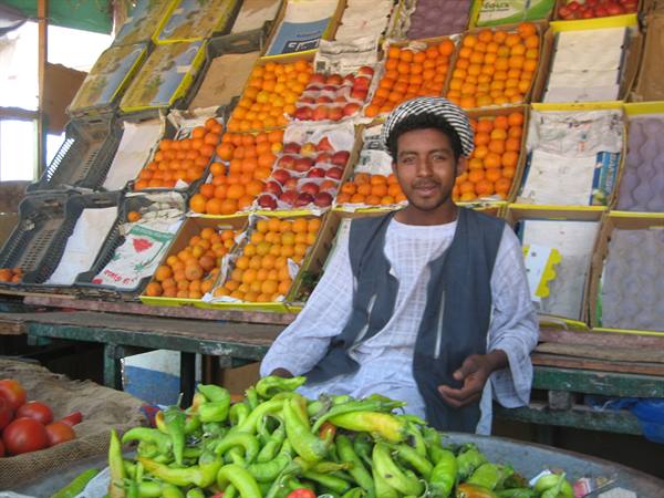 Fruit vendor in front of orange crates and green peppers at market