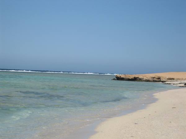 Pale sand, turquoise water and offshore reef under clear sky