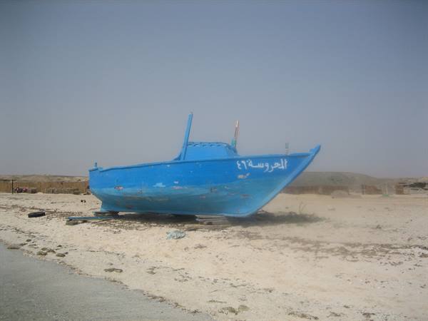 Blue fishing boat beached on sand, Arabic name painted on hull