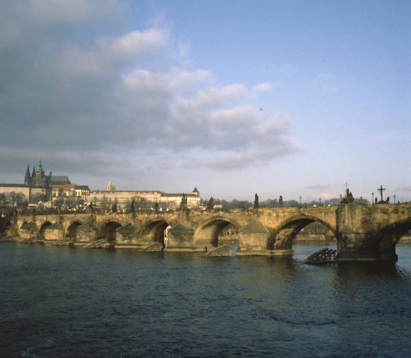Charles Bridge in Prague, stone arches over the Vltava, castle under clouds