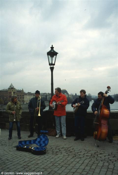 Street musicians performing on Charles Bridge, cloudy sky, open case for coins