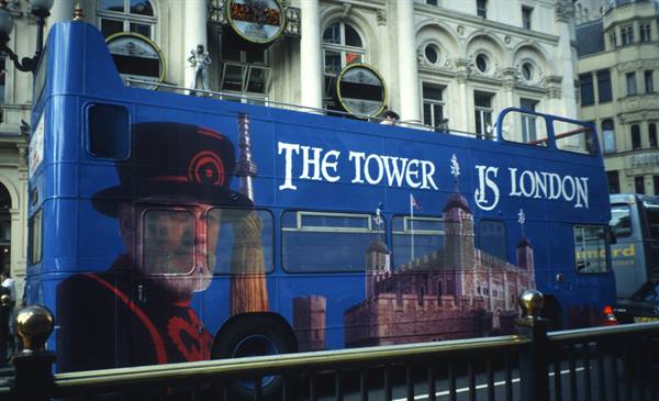 Blue double-decker bus advertising the Tower of London on a city street