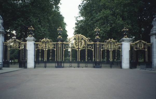 Ornate golden wrought-iron gate with stone pillars, Buckingham Palace, soft daylight