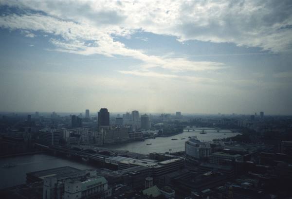 The Thames winding between London bridges and skyscrapers under scattered clouds