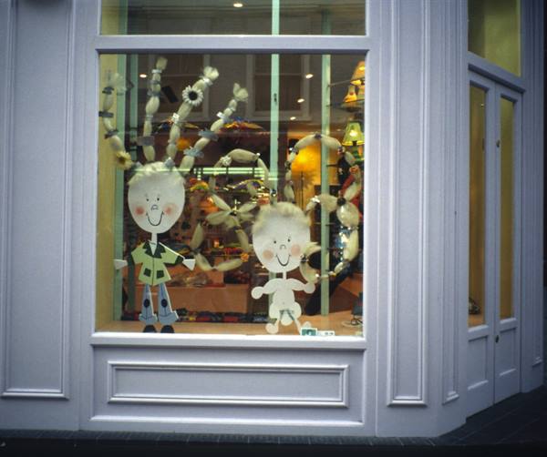 White shop window with two smiling paper dolls and wool decorations