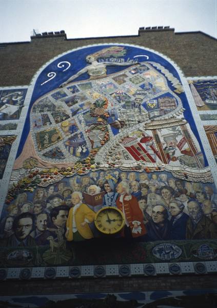 Large colorful mosaic on brick facade, with yellow clock and historical figures