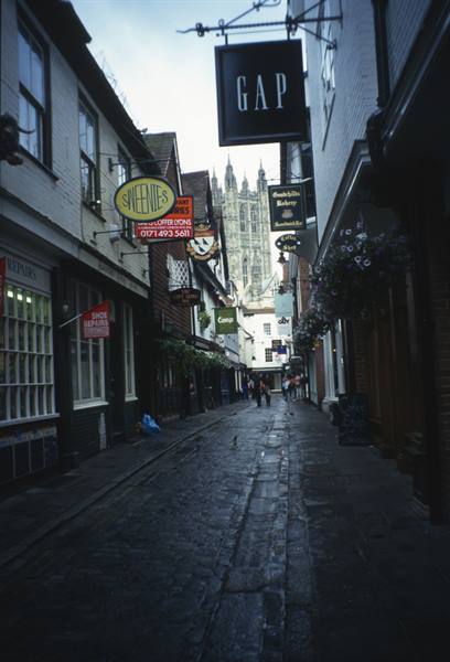 Cobbled street with shop signs and pedestrians, Canterbury Cathedral towering in the background