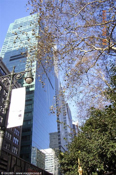 Green glass skyscrapers and lamppost among bare branches in Bryant Park, New York