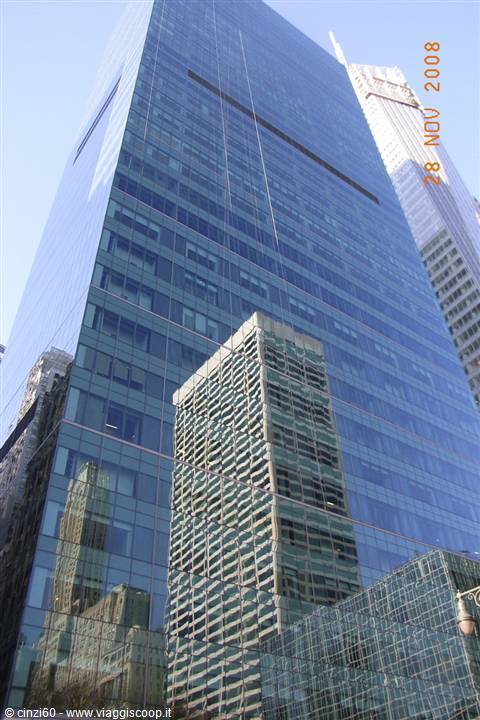 Blue glass skyscraper reflecting nearby towers under bright sunlight