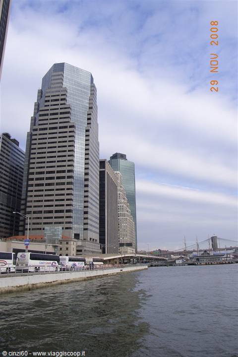 Glass skyscrapers along Lower Manhattan pier, buses parked, Brooklyn Bridge in background