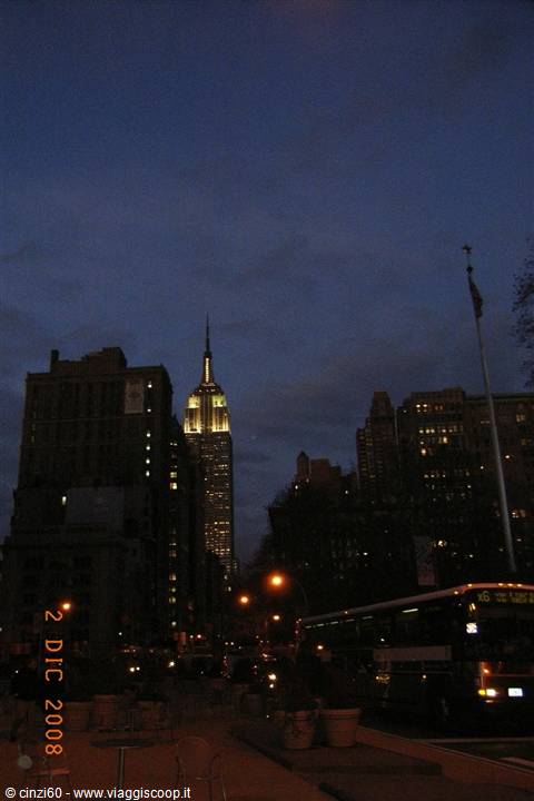 The Empire State Building lit up at night among Manhattan skyscrapers, a bus in the foreground