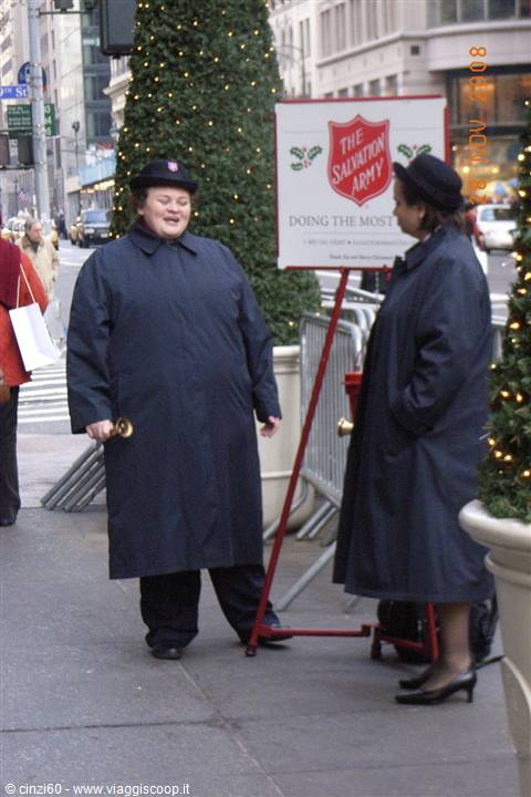 Two Salvation Army volunteers with bells on a Christmas-decorated New York sidewalk