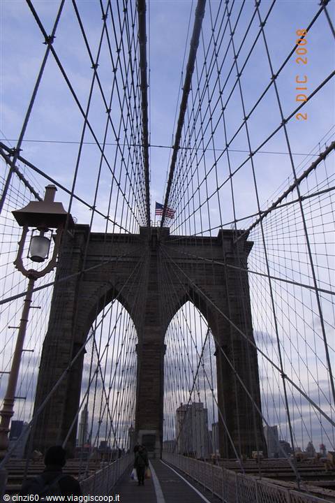 Stone tower of Brooklyn Bridge amid steel cables, American flag, lamppost