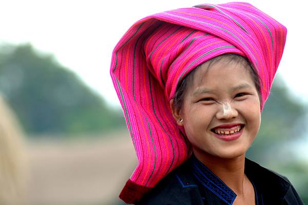 Smiling girl wearing a striped pink headwrap, blurred green background