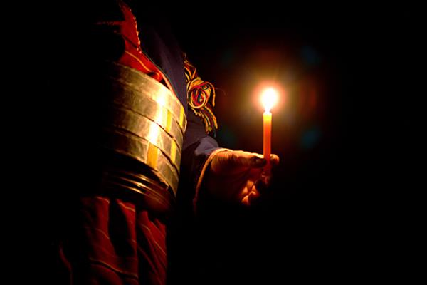 Person in traditional dress with metal belt holding a lit candle