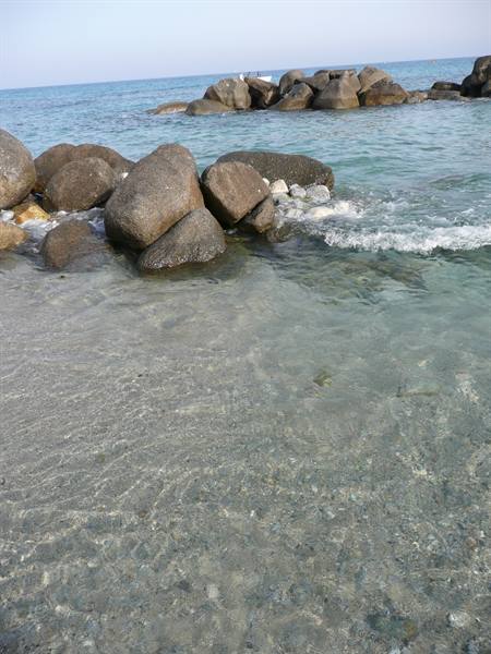 Clear water over sand and large boulders, a dinghy on the sea