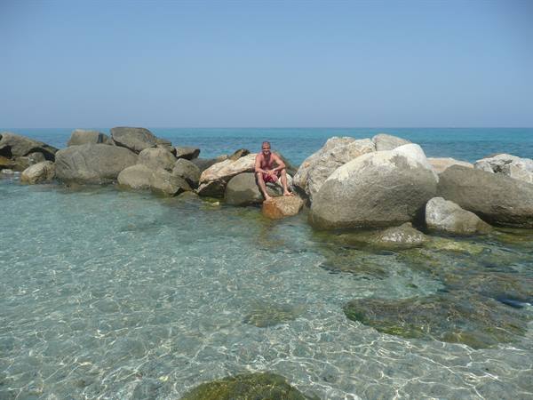 Man sitting on a large granite rock surrounded by clear turquoise water