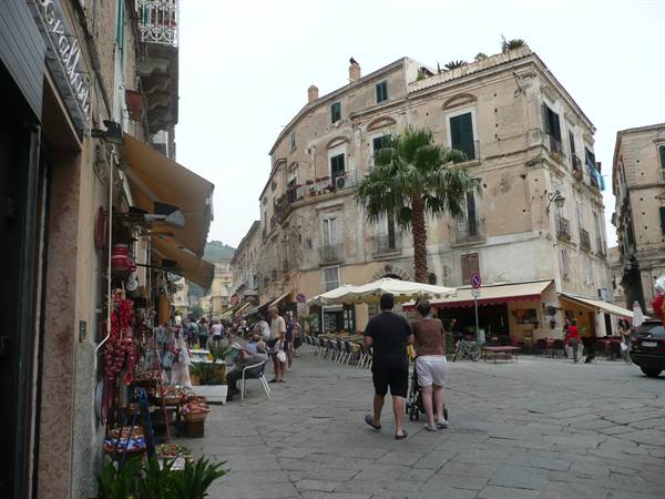 Square with palm tree, old buildings and market stalls under grey sky