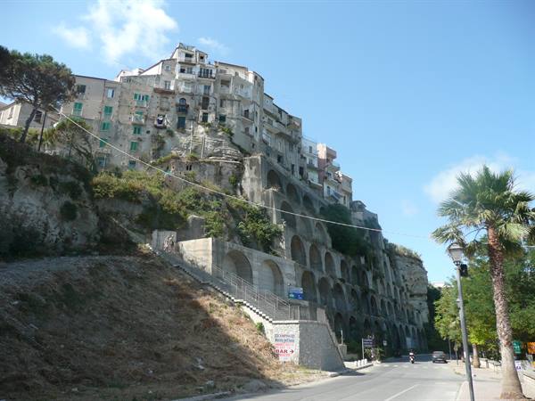 Old stone houses on rock with arches, palm trees, sunny sky, Tropea