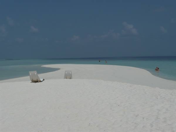 Two lounge chairs on white sand of a sandbank, turquoise water
