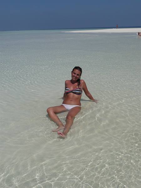 Woman in bikini sitting in clear turquoise water over white sand