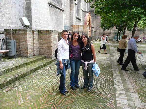 Three friends pose beside Seville Cathedral on the brick paved ground