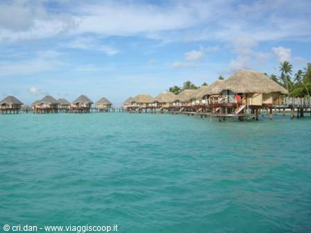 Thatched overwater bungalows on stilts above the turquoise lagoon, cloudy sky