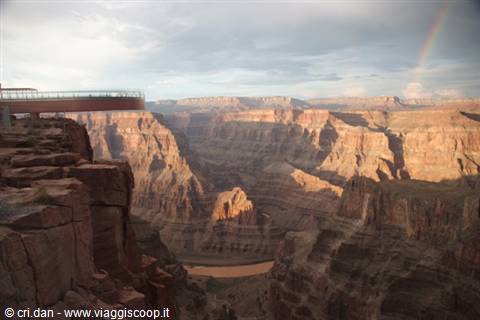 Glass Skywalk bridge overlooking the Grand Canyon rocky cliffs, rainbow in sky