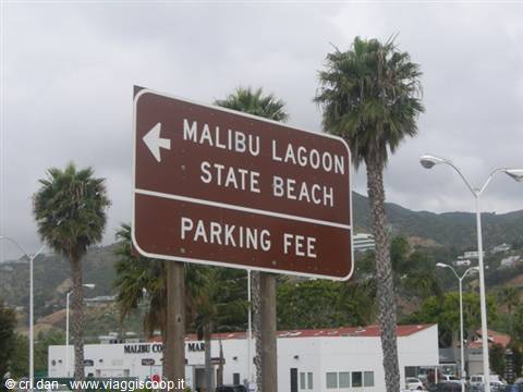 Brown Malibu Lagoon State Beach sign among palm trees and gray sky
