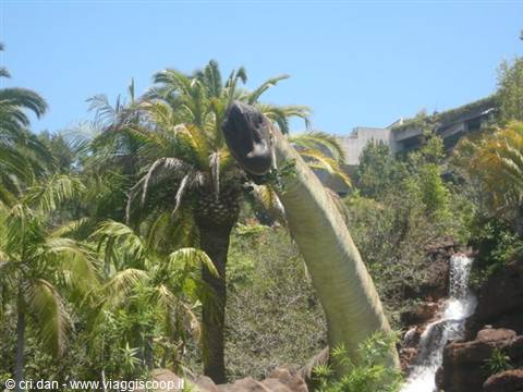 Dinosaur statue among palm trees and artificial waterfall at Universal Studios Hollywood