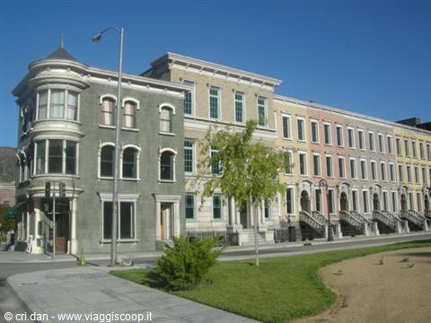 Row of colorful Victorian houses with stoops along a street and lawn