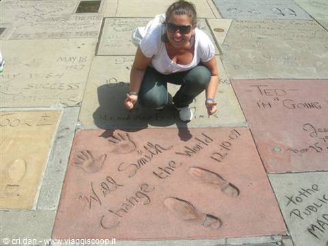 Woman crouching next to Will Smith's handprints at Grauman's Chinese Theatre