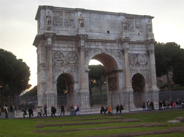 Tourists walk along the fence of the marble Arch of Constantine, Rome
